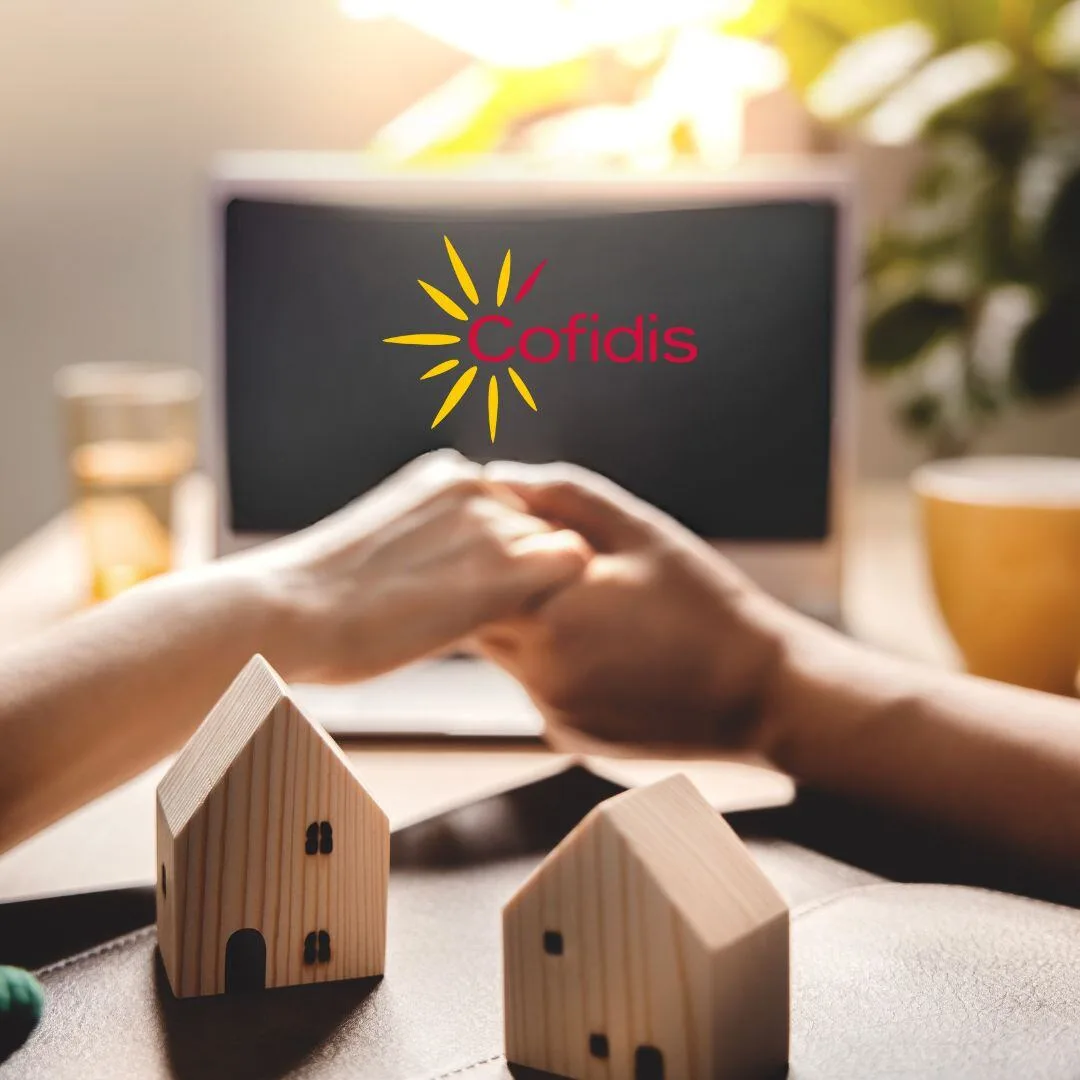 Twee mensen schudden elkaar de hand aan een bureau met houten huisjes en het Cofidis-logo